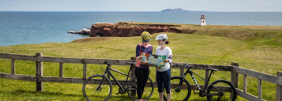 Two cyclists looking at a map at the base of the Cap Alright lighthouse, in Havre-aux-Maisons, Îles de la Madeleine