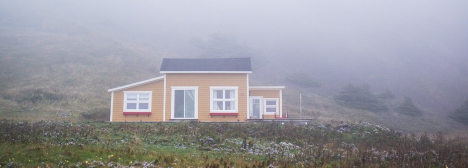 Petite maison jaune en bas d'une butte, dans la brume