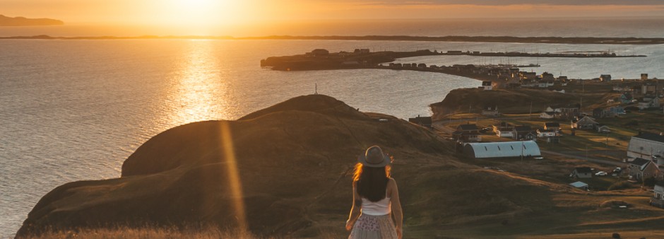 A woman gazes at the rising sun over the sea from the Demoiselles Nature Reserve in Havre-Aubert, Îles de la Madeleine. In the background, you can see the La Grave heritage site and Entry Island.