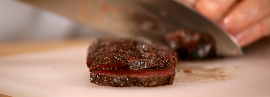 A chef slicing a piece of seal meat on a cutting board